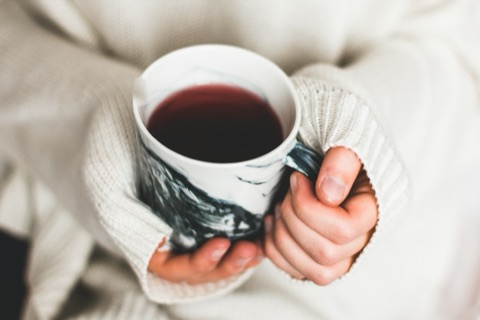 Mains en pull crème refermées sur une tasse de thé fumante